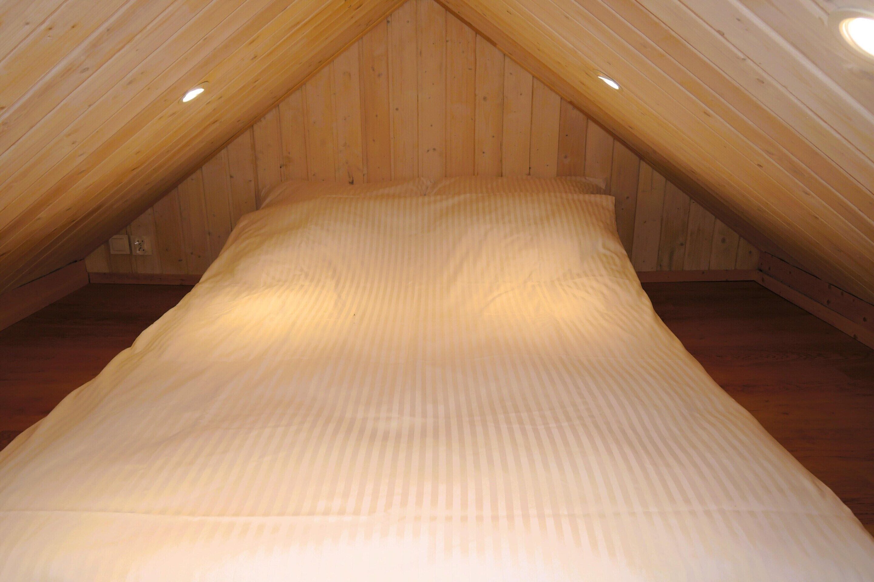 A narrow, sloped ceiling room with wooden walls and a bed with a striped bedspread.