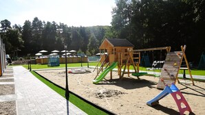 A playground with a wooden playhouse, a slide, and a climbing structure. - Holiday Homes With Swimming Pool, Close to the sea (Międzyzdroje)