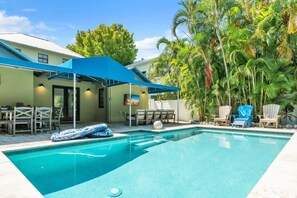 A swimming pool with lounge chairs and umbrellas, surrounded by palm trees and a covered patio area. - Chilli Fish 4 Bedroom Home (Anna Maria)
