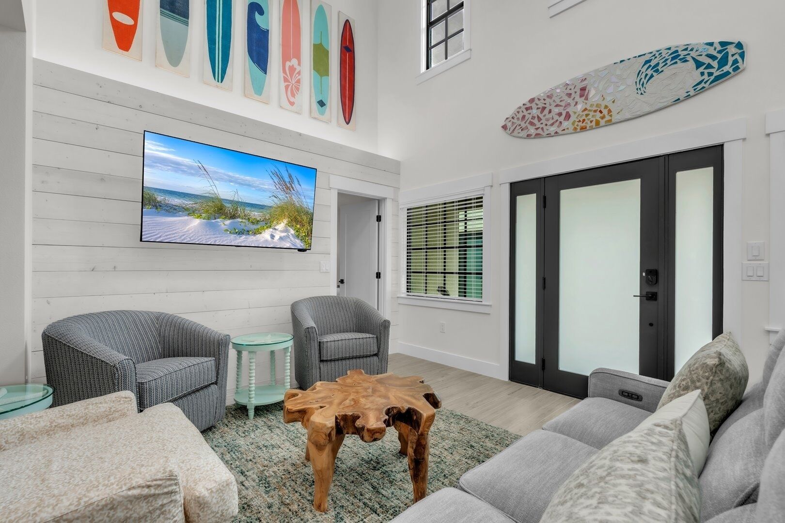 A modern living room with a large TV, two grey armchairs, a wooden coffee table, and a grey sofa.