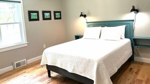 Ein Schlafzimmer mit einem Bett, zwei Wandlampen, einem Fenster und drei gerahmten Bildern an der Wand.