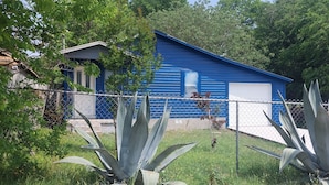 Un bâtiment bleu avec une porte de garage, entouré d’une clôture en treillis métallique et de grands plants d’agave.