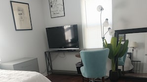 Une chambre à coucher avec un lit, une télévision, une chaise et une fenêtre avec des stores.