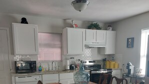 Une cuisine avec des meubles blancs, un four à micro-ondes, une cuisinière et une table à manger avec des chaises.