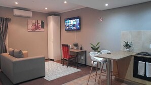 Ein modernes Wohnzimmer mit einer Couch, einem Essbereich mit Tisch und Stühlen, einer Küche mit Herd und einem an der Wand befestigten Fernseher.