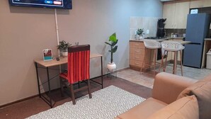 Ein kompakter Wohnraum mit einer Küchenzeile, einem Essbereich mit zwei Barhocker, einer Couch und einem an der Wand montierten Fernseher.
