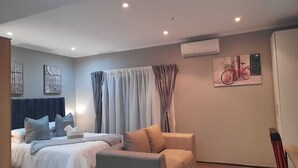 Ein modernes Hotelzimmer mit Bett, Sofa, einem Fenster mit Vorhängen, einer Klimaanlage und einem Wandbild eines Fahrrads.