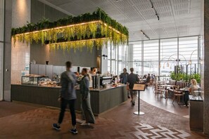 Un espacio interior moderno con una barra central, zonas de estar y grandes ventanales.