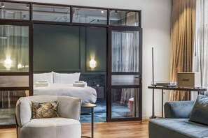 A hotel room with a bed, a seating area with a chair and a sofa, a small table with a lamp, and a view through a glass door. - Chic & Spacious – Ideal for Business & Leisure (Auckland City)