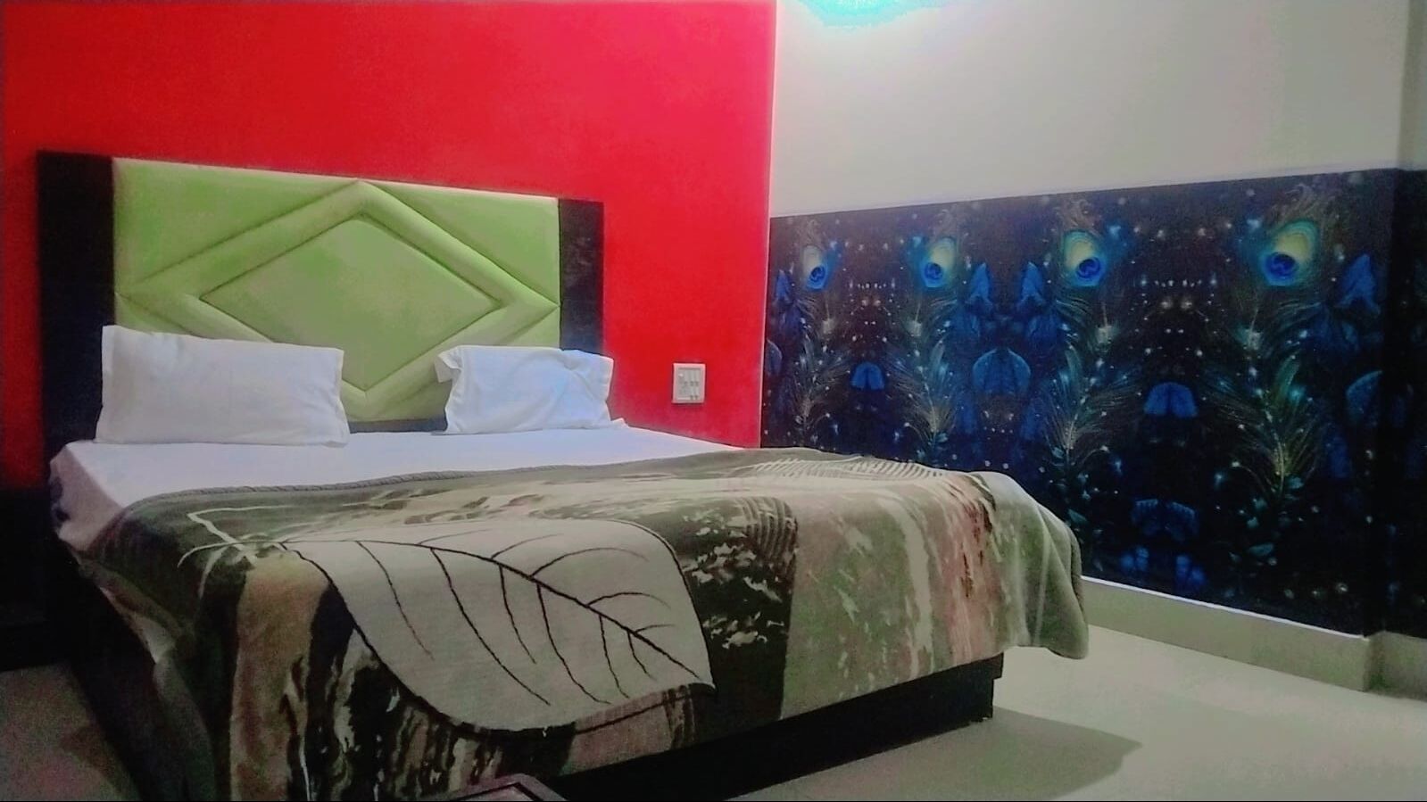 A room with a bed, a green pillow, a white pillow, and a peacock-themed tapestry on the wall.