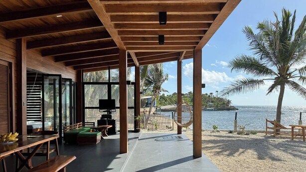 Un espacio al aire libre techado, con techo de madera, zona de estar con bancos y vista al mar.