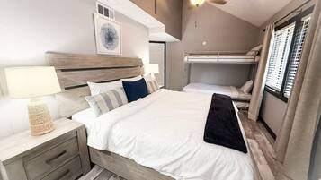 Un dormitorio con cama, mesitas de noche, ventilador de techo y ventana con cortinas.