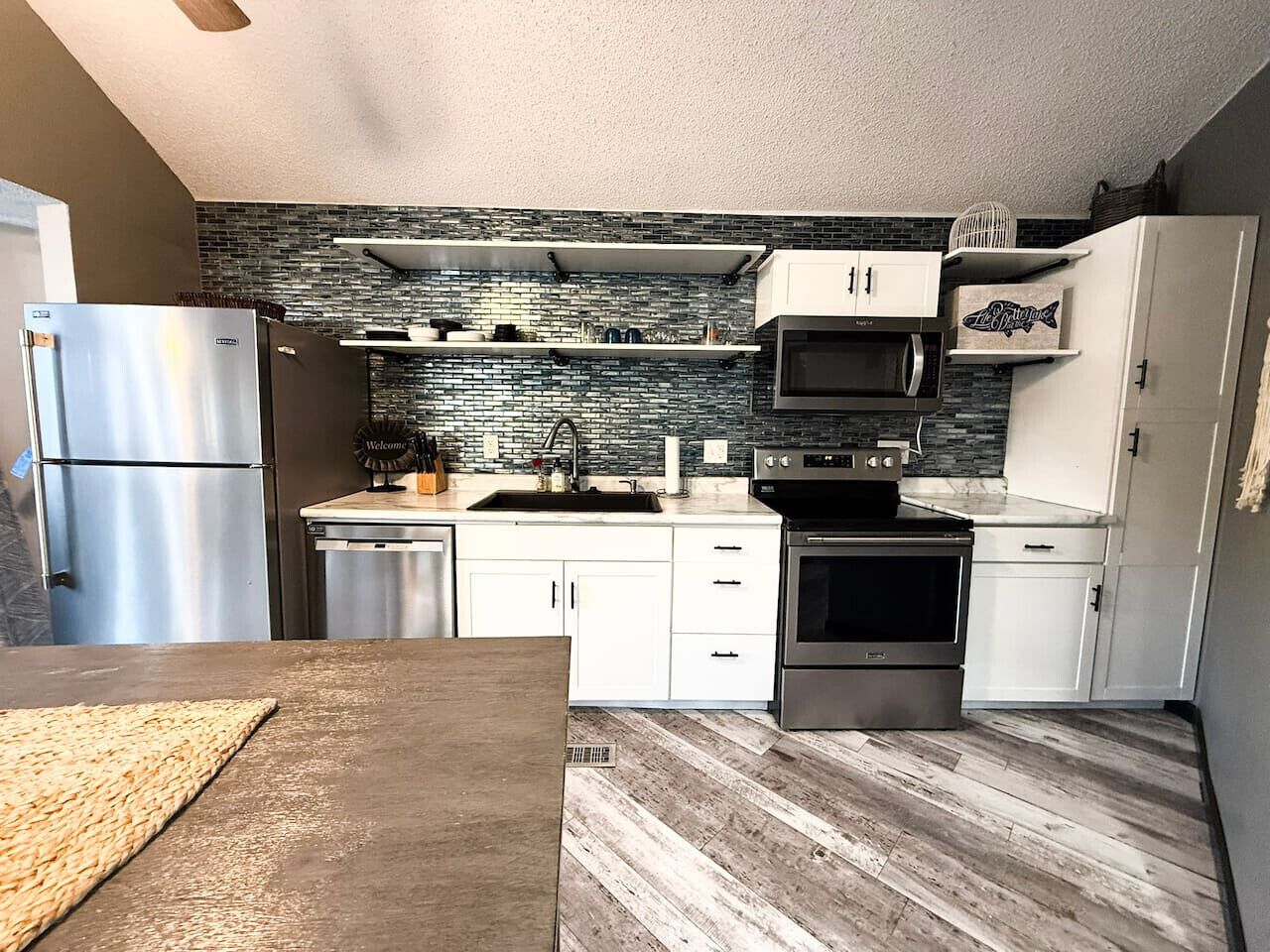 A modern kitchen with white cabinets, a stainless steel refrigerator, a microwave, and a stove.
