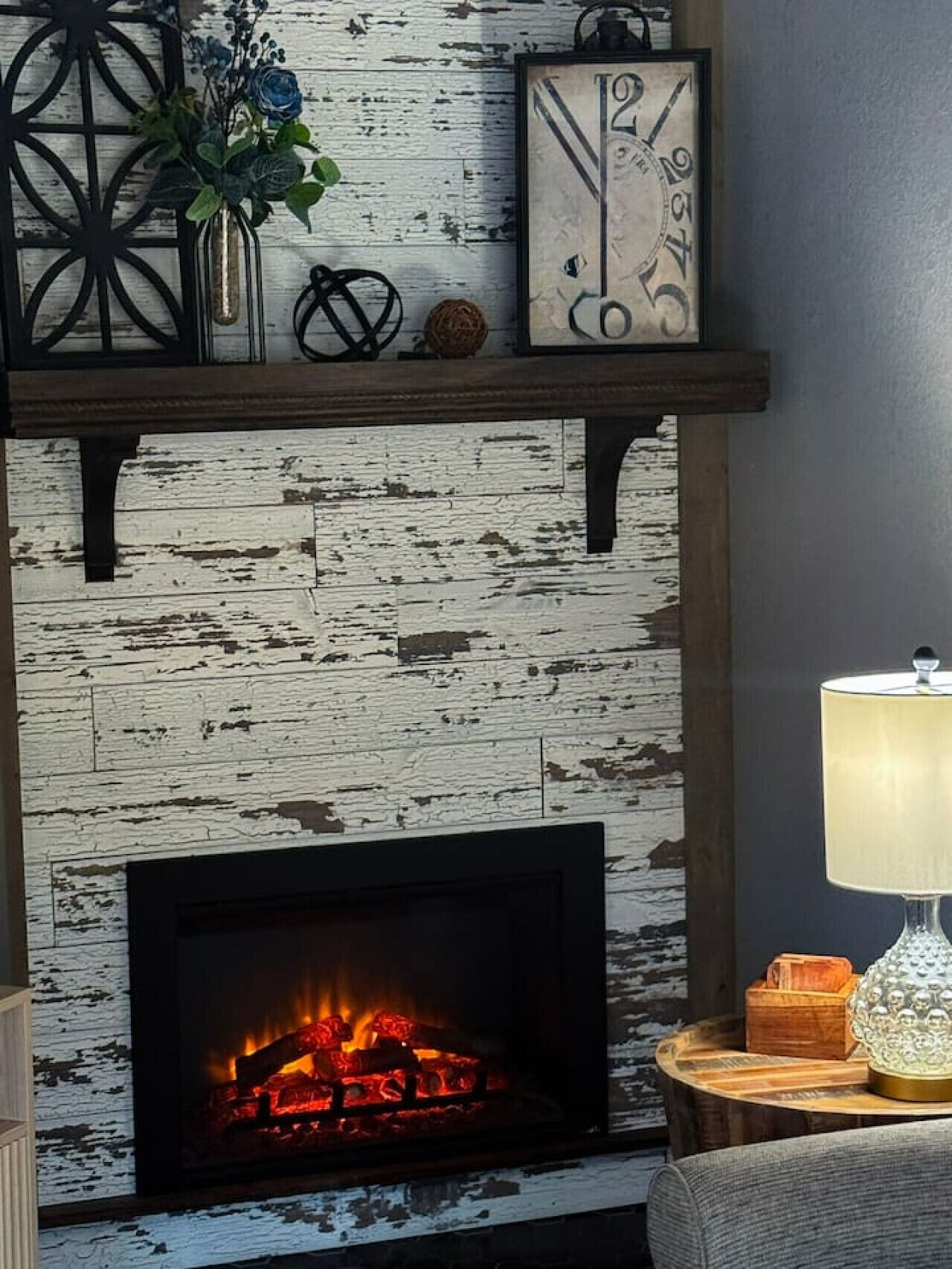 Una chimenea rústica con fuego, un reloj de pared decorativo y un florero con flores sobre la repisa.