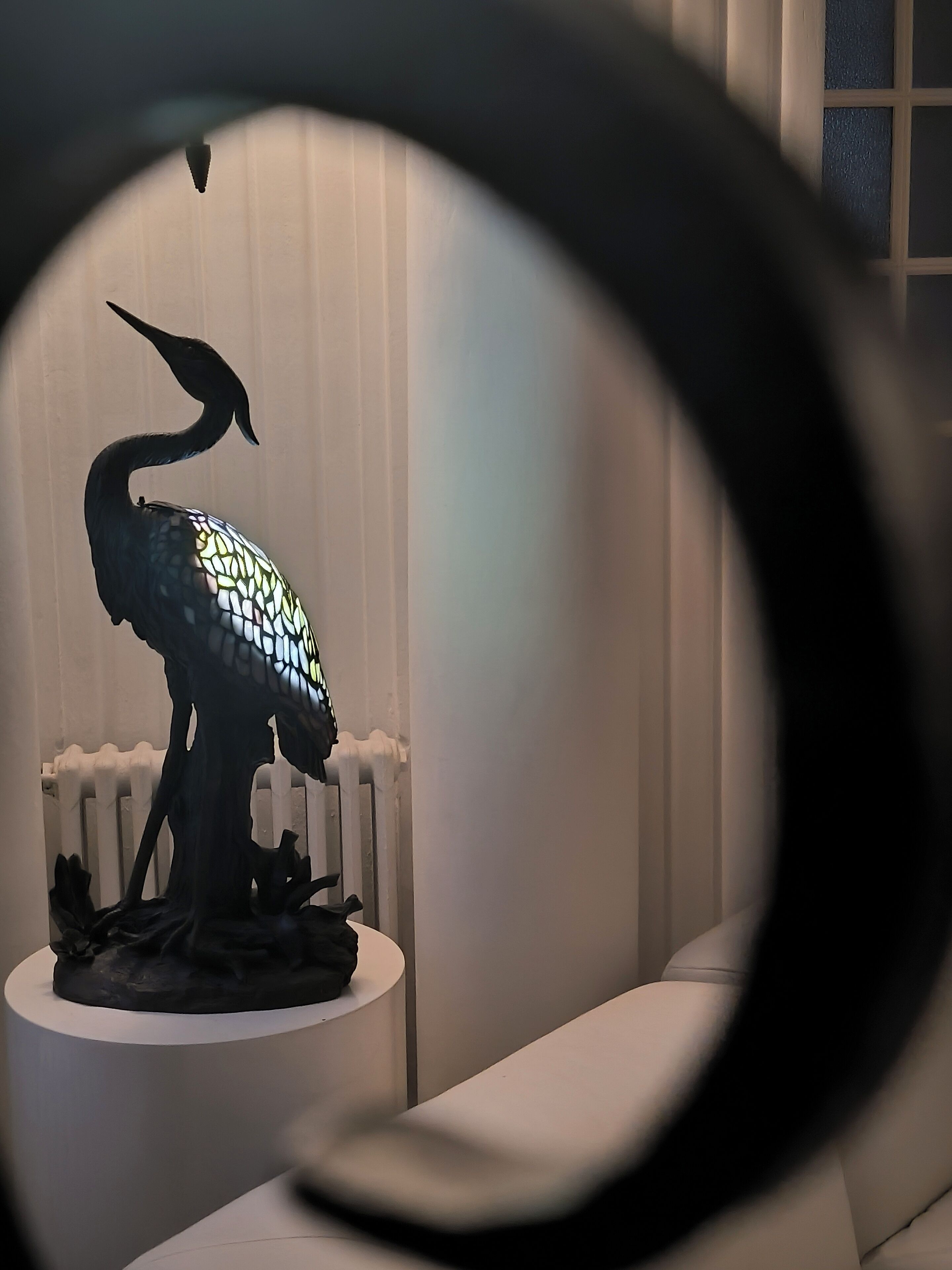 A sculpture of a bird on a pedestal in a room with white walls and a radiator.