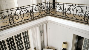 A spacious, elegantly designed interior with a high ceiling, a decorative railing, a patterned floor, and a seating area with a white sofa and decorative lamps. - Chambre d'hôtes in Demeure Remarquable / independent entrance (Béziers)