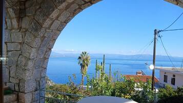 A stone archway overlooking a coastal view with buildings and a palm tree.