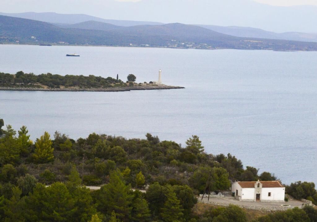 A coastal landscape with a lighthouse, a small white building, and a ship in the distance.
