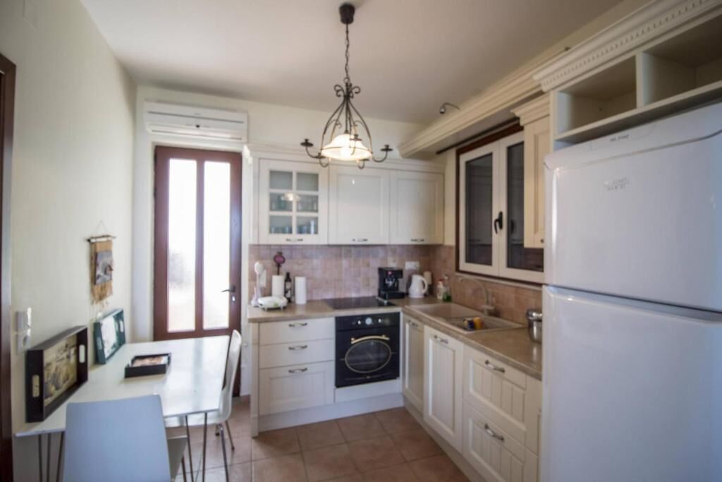 Een compacte keuken met witte kastjes, een ingebouwde oven, een koelkast, en een eethoek met een tafel en stoelen.