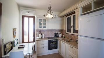 Een compacte keuken met witte kastjes, een ingebouwde oven, een koelkast, en een eethoek met een tafel en stoelen.