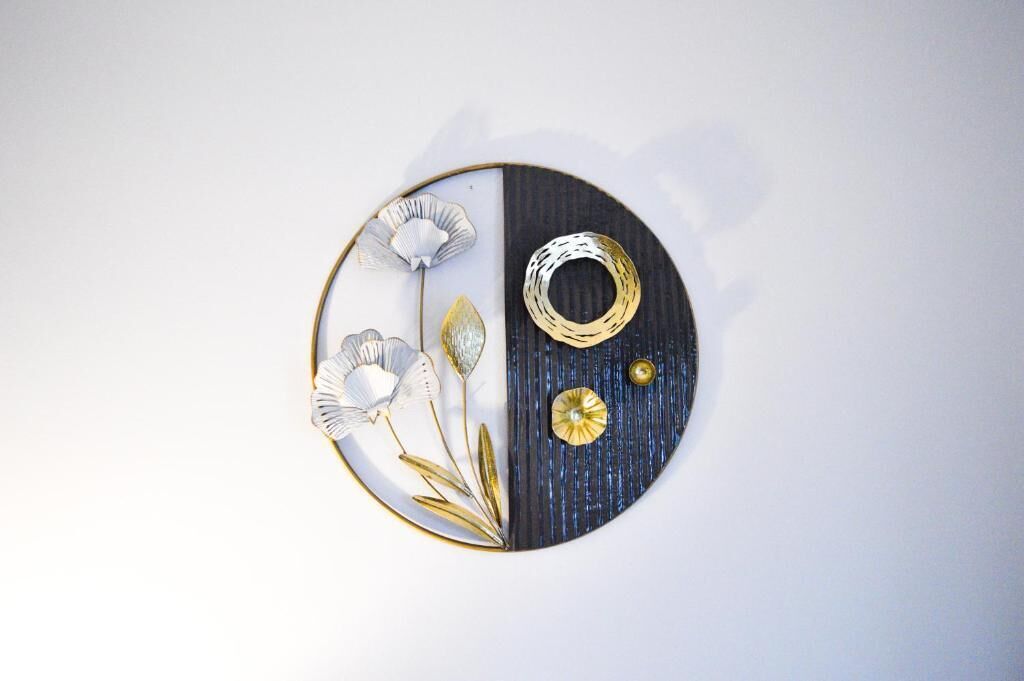 A circular wall decoration with a split design, featuring a floral arrangement and a ring on one side.