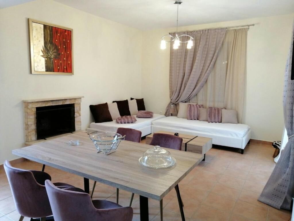 Ein modernes Wohnzimmer mit Kamin, einem Esstisch mit Stühlen, einer Couch und einem großen Fenster mit Vorhängen.