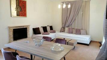 Ein modernes Wohnzimmer mit Kamin, einem Esstisch mit Stühlen, einer Couch und einem großen Fenster mit Vorhängen.