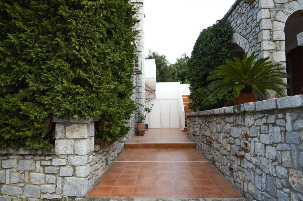 A stone-walled pathway leading to a white door, surrounded by lush greenery.