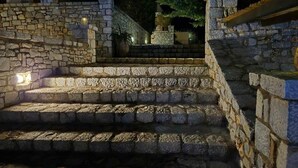 A stone staircase leading up to a building entrance, surrounded by stone walls and illuminated by wall-mounted lights. - Malvazios Villas (East Mani)