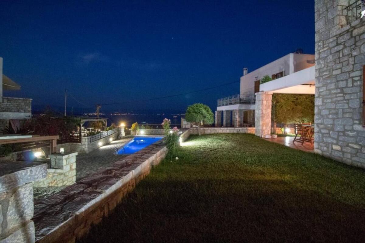 Une villa moderne dotée d’une piscine, de murs en pierre et offrant une vue sur la mer la nuit.