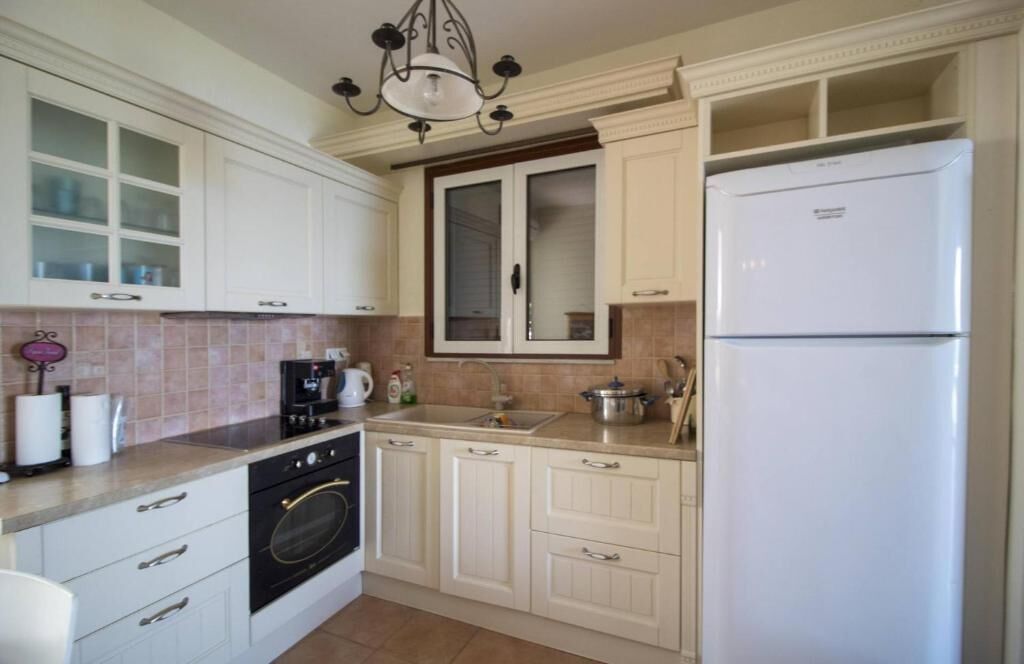 A kitchen with white cabinets, a built-in oven, a refrigerator, and a chandelier.