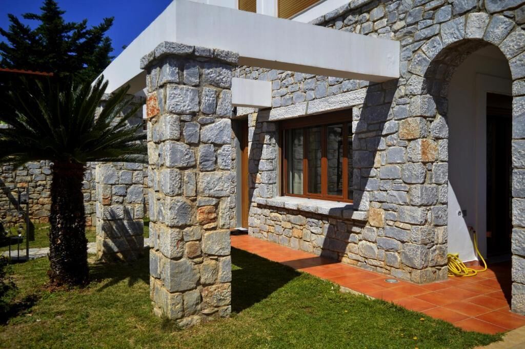 Um edifício de pedra com janela e porta, rodeado por relva e uma palmeira.