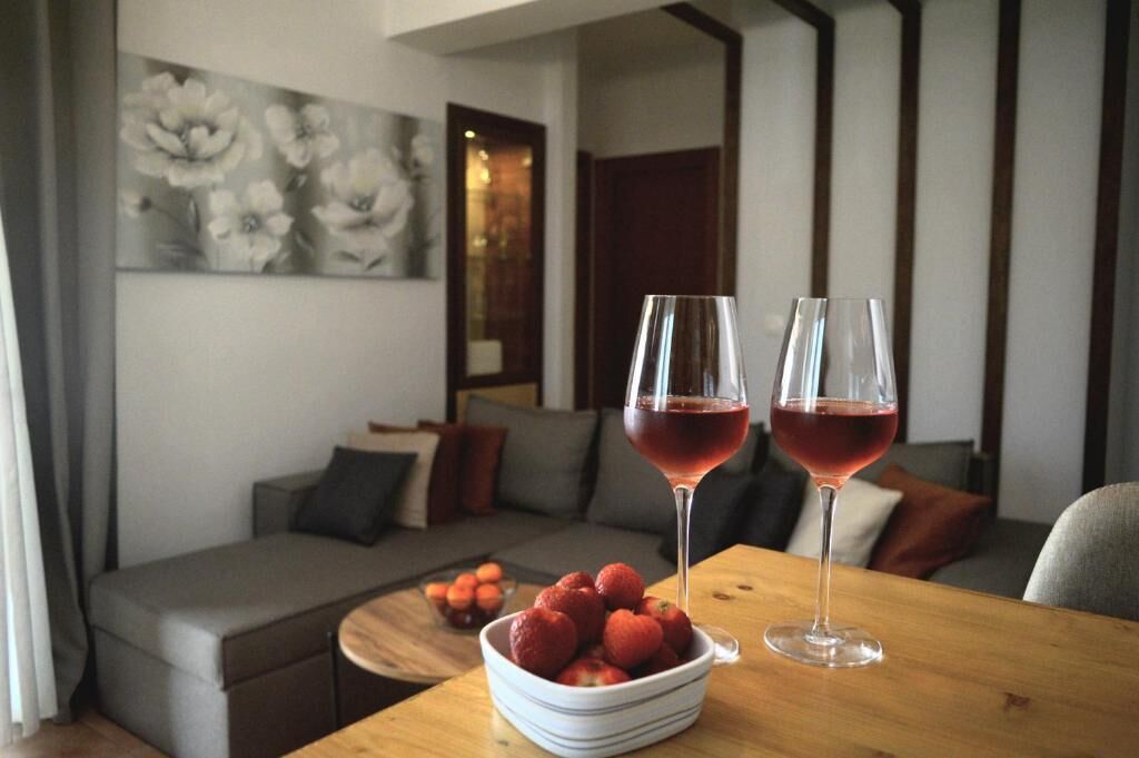 A modern living room with a sofa, a table with a bowl of strawberries, and two glasses of red wine.
