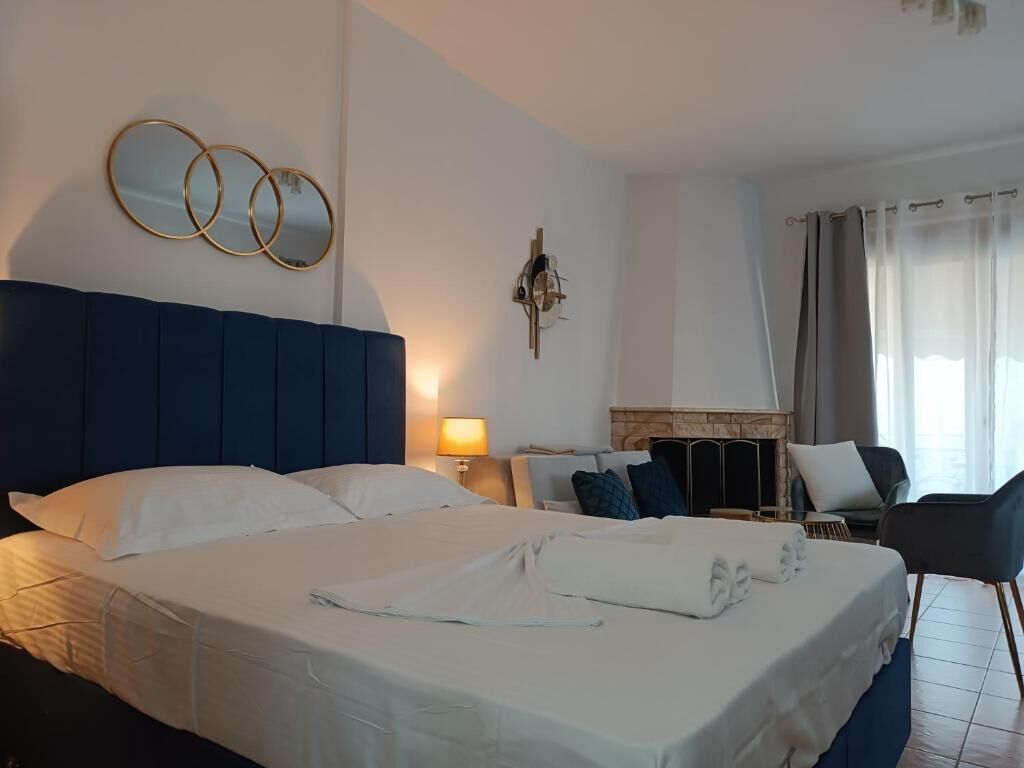 Habitación de hotel con una cama grande, un espejo montado en la pared, una chimenea y una zona de estar con una silla y una mesa.
