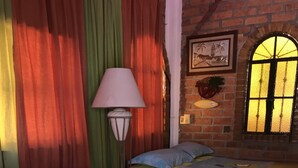 A room with two beds, a lamp, and a window with a brick wall and a framed picture. - 🎥✨ Imagine waking up to the sound of the sea, a cup of coffee on the terrace. (Puerto Vallarta)