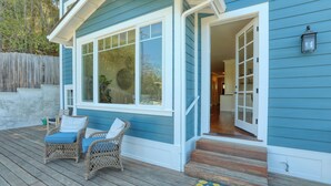 Ein blaues Haus mit einer Veranda, zwei Korbstühle mit Kissen und einer Holztreppe zum Eingang.