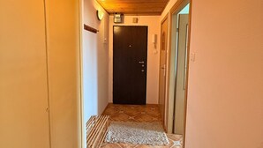 Un couloir étroit avec un plafond en bois, une porte noire au fond et un sol à motifs.