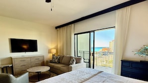 Une chambre d’hôtel avec un grand lit, un canapé, une télévision, un bureau et un balcon donnant sur la plage.