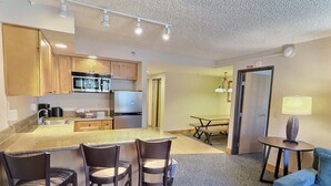 A modern kitchen with a central island, bar stools, a dining table, and a blue sofa. - Grand Lodge Crested Butte #425 | Walk to Lifts | Sleeps 6, Hot Tub (Crested Butte)