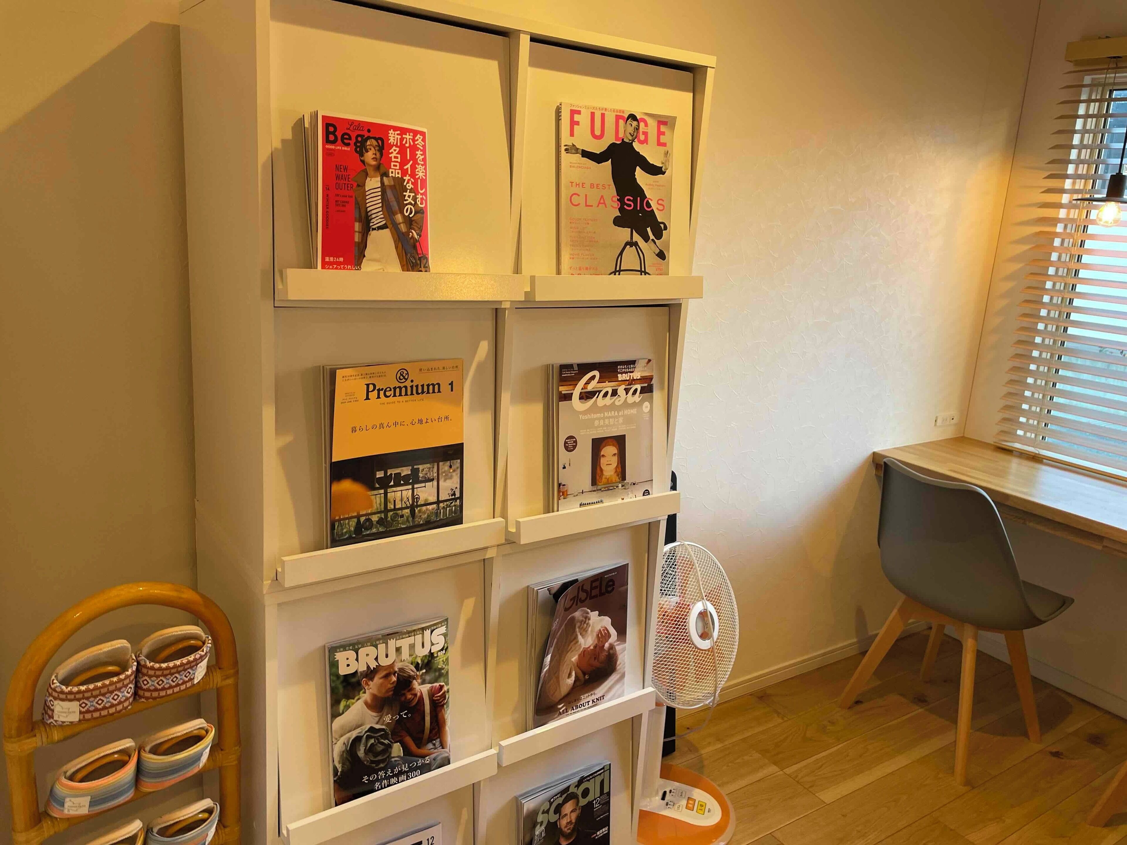Une pièce avec une étagère blanche où sont exposés des magazines, ainsi qu’une petite chaise en bois.