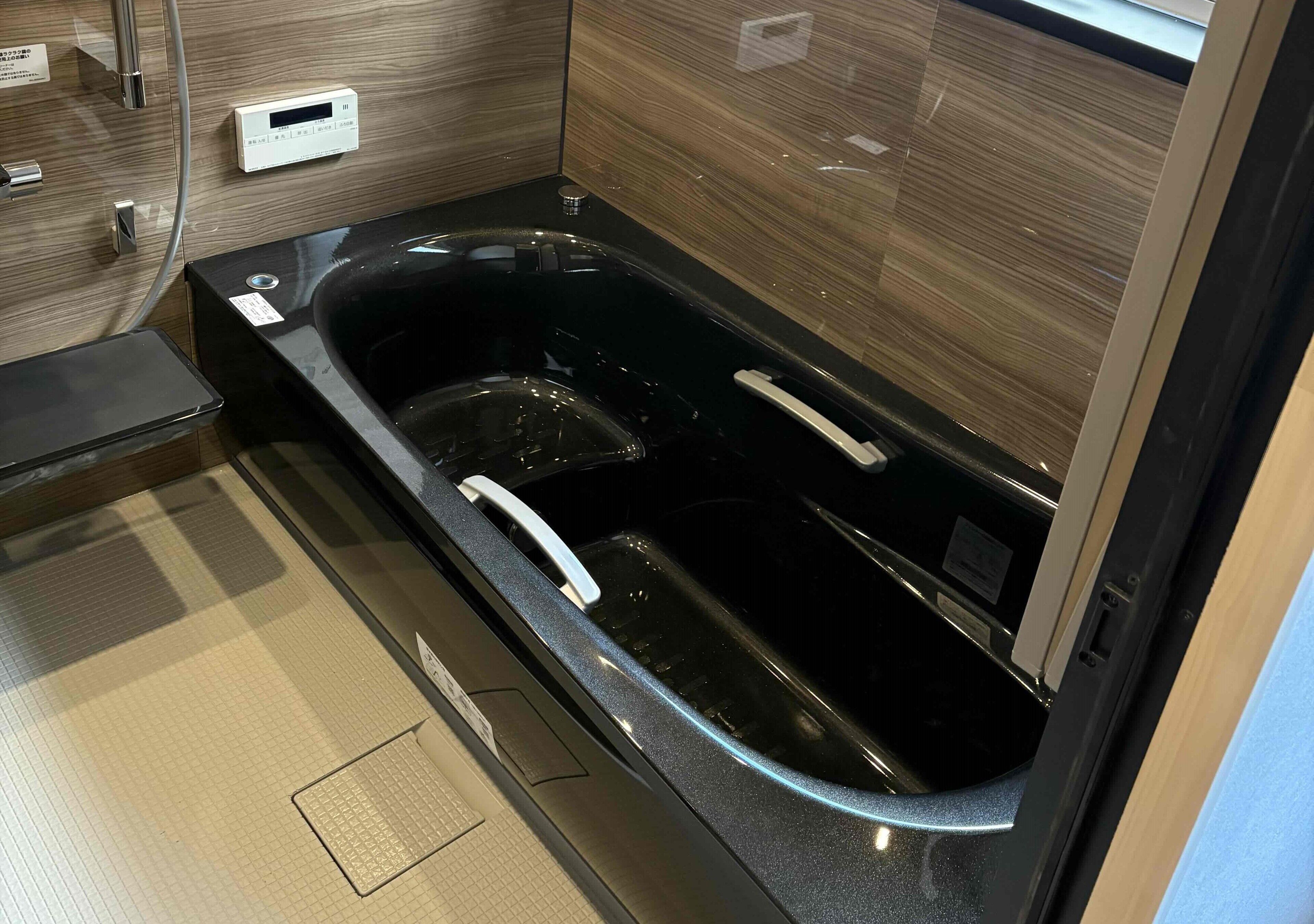 A modern bathroom with a black bathtub, a control panel, and a glass shower enclosure.