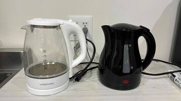 Une bouilloire électrique blanche de la marque HAGOOGI et une cafetière électrique noire de la marque FUJILIFE, posées sur une surface en bois.