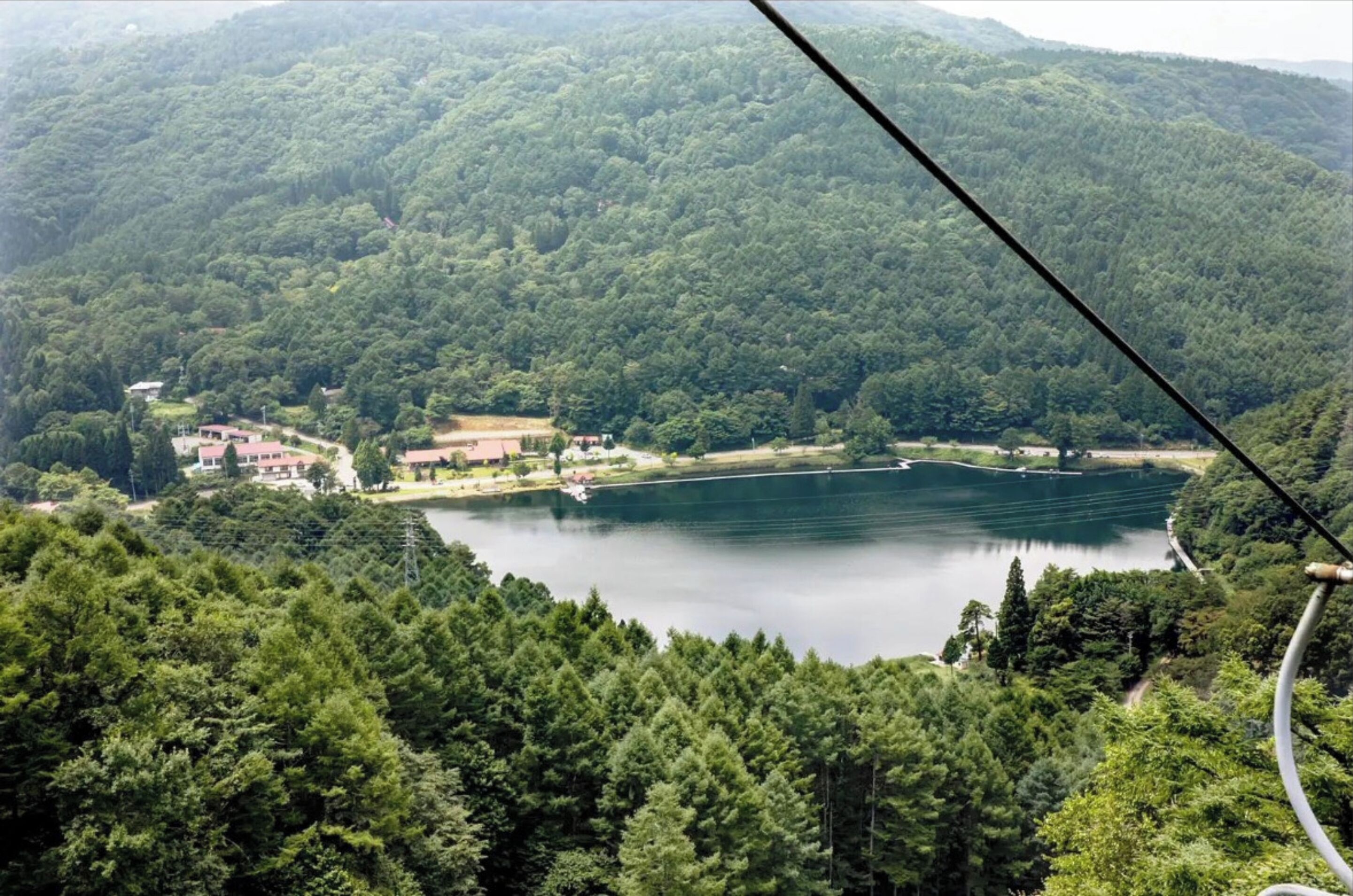 Un lago rodeado de bosque denso, con edificios y un bote amarrado a la orilla.