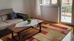 A living room with a sofa, a coffee table, a rug, and a window with a view of buildings. - Seaside Apartment Bubi (Crikvenica)