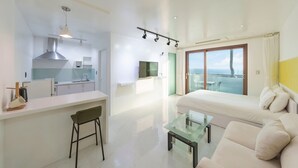 Een moderne hotelkamer met een kitchenette, een glazen eettafel, een bank en een balkon met uitzicht.