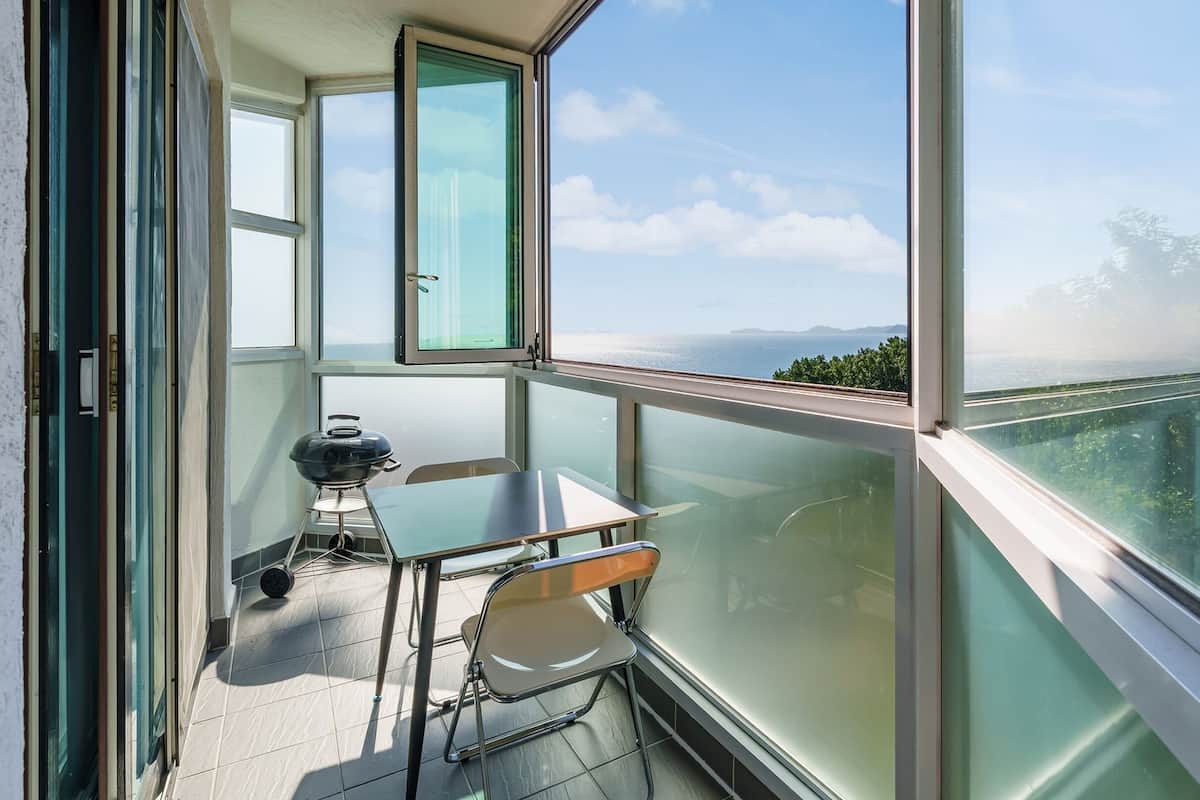 Un balcon avec une table et des chaises, un barbecue et une vue sur la mer et la verdure.