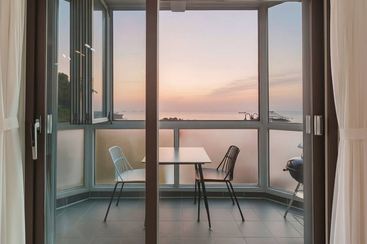 Un balcon avec vue sur la mer, une table, deux chaises et un barbecue.