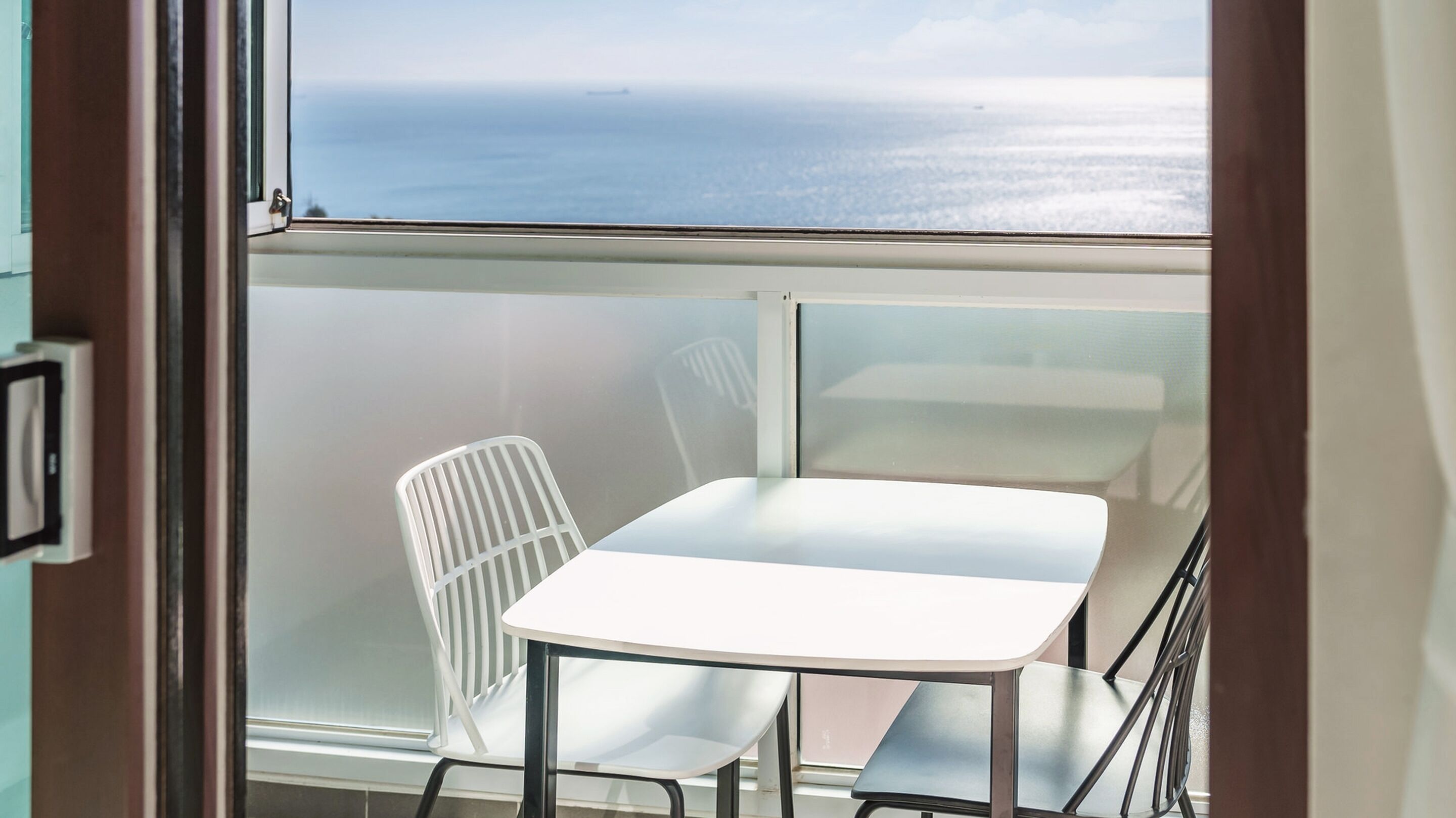 Un balcon avec une table et des chaises blanches, donnant sur la mer.