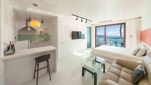 Een modern appartement met kitchenette, eethoek, woonkamer met een bank en glazen salontafel, en een balkon met uitzicht.