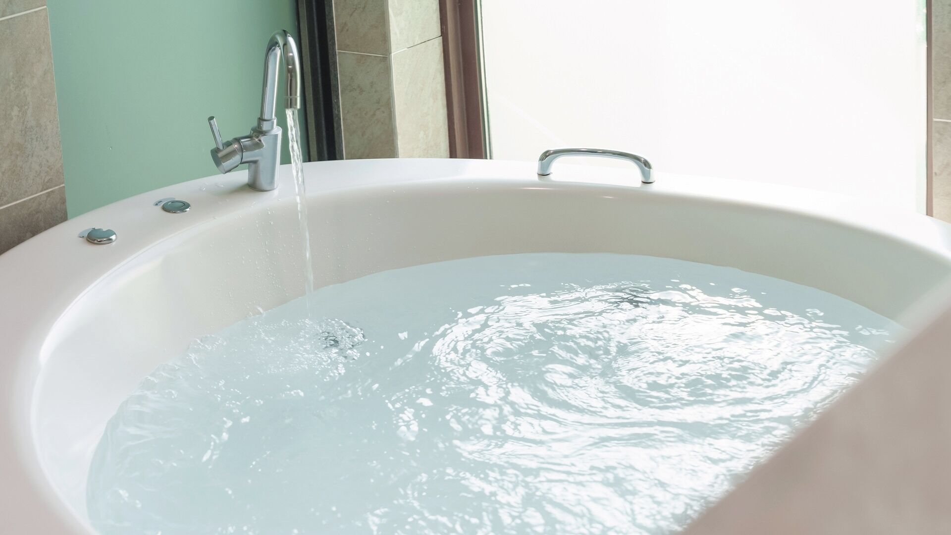 A bathtub with running water, a faucet, and a window in the background.